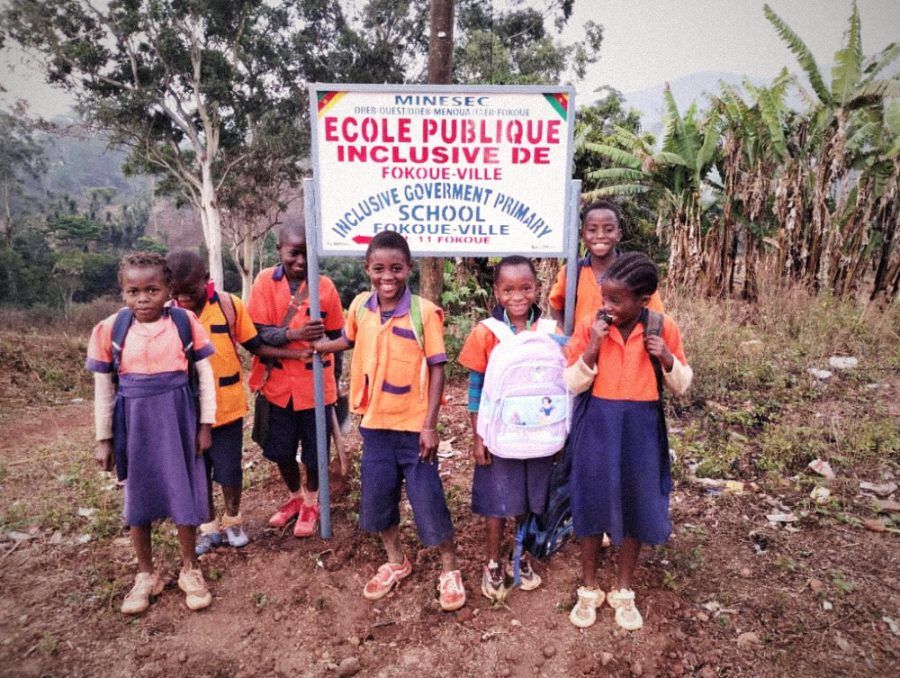 Sept élèves, cartables sur le dos, sous le panneau de l'École publique inclusive de Fokoué-Ville