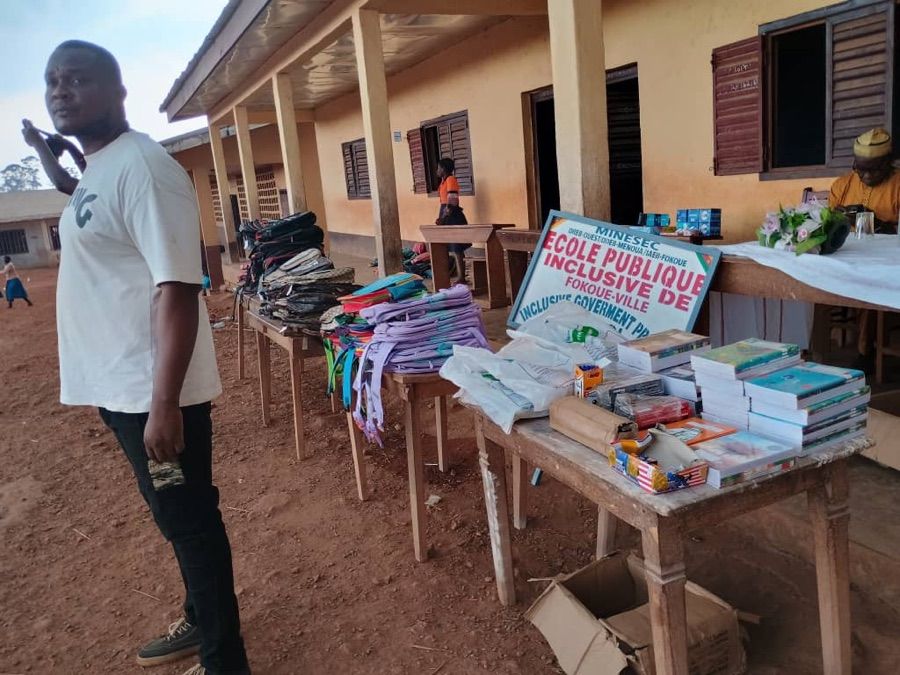 Un membre de MAMIKEU devant les tables où sont disposés cartables, cahiers et fournitures, sous la véranda de l'école